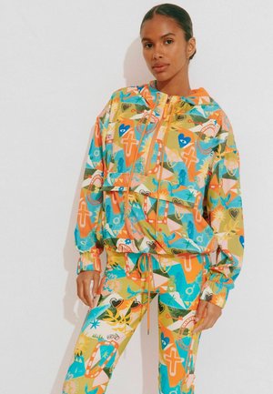 Colorful tracksuit featuring a hooded zip jacket and matching pants. Made of lightweight material with geometric patterns in orange, green, and blue.