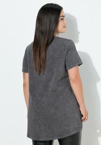 Camiseta gris de gran tamaño con una tela suave y texturizada, mangas cortas y un dobladillo redondeado. La parte posterior presenta un corte relajado y un diseño minimalista.