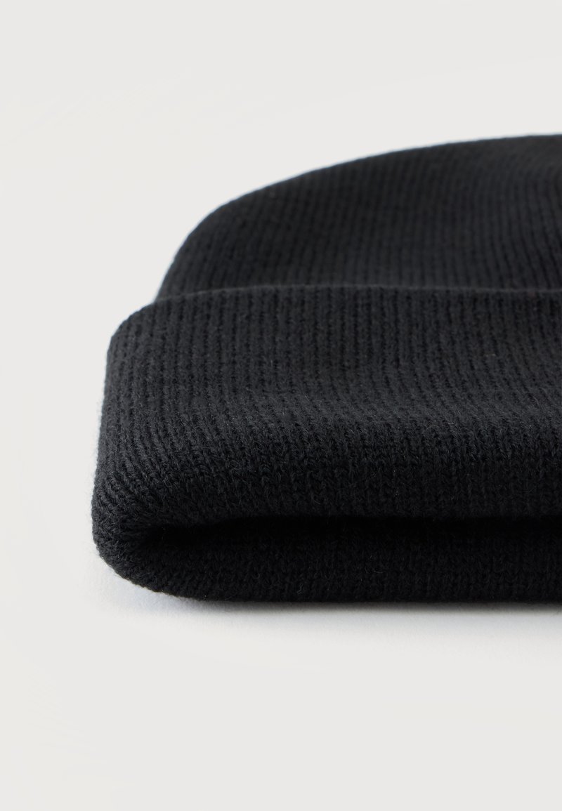 Gorro beanie negro de punto acanalado doblado sobre un fondo liso y claro.
