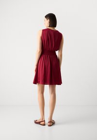 Robe courte bordeaux avec un corps ajusté et une jupe évasée, dotée d'une taille élastique. Tissu lisse et léger avec une texture minimale.