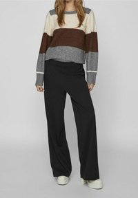 Sweter w paski w kolorze kremowym, brązowym i szarym; szerokie czarne spodnie; jasne buty na platformie; prążkowane mankiety i dół.