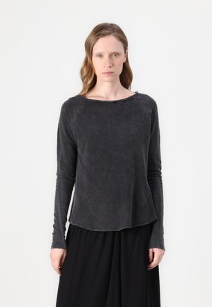 Débardeur à manches longues et col rond en gris foncé, fabriqué dans un tissu doux. Doté d'un ourlet brut et d'une finition texturée, associé à une jupe noire fluide.