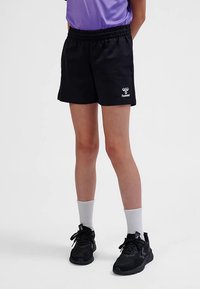 Schwarze Sportshorts mit elastischem Bund, versehen mit einem dezenten weißen Logo. Kombiniert mit schwarzen Sneakern und weißen Socken.