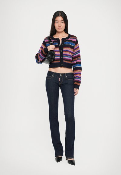 Cárdigan de punto corto multicolor con rayas horizontales. Jeans de mezclilla oscuros de pierna acampanada. La modelo lleva una pequeña bolsa negra.