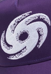 Violetinė kepurė su išsiskiriančiu baltu siuvinėtų sūkuriniu logotipu. Audinys yra tekstūruotas, su siuvinėjimo raštu ir kontrastingomis siūlėmis.