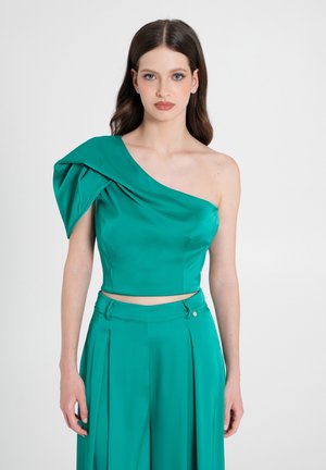 Top turchese a spalla unica in tessuto morbido con manica drappeggiata. Design cropped, silhouette minimalista, abbinato a pantaloni plissettati coordinati.