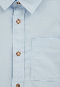 Světle modrá košile na knoflíky vyrobená z texturované tkaniny, s hnědými knoflíky a náprsní kapsou se viditelnými detaily šití.