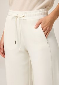 Pantaloni da jogging bianchi con vita elastica, cordoncino con dettagli in argento e tasche laterali realizzati in un tessuto morbido.