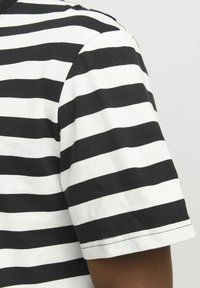 Sort/hvid stribet t-shirt lavet af bomuld, med korte ærmer, rund hals og synlige sømdetaljer langs kanten.