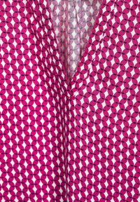 Rosa tyg med ett geometriskt mönster av diamanter i vitt med svarta accenter, som visar en mjuk textur och V-ringning.