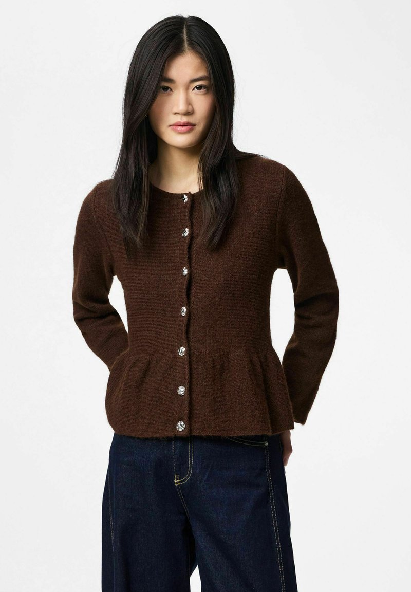 Cardigan marron texturé avec un ourlet à basque, manches longues et boutons argentés sur le devant, assorti à un jean foncé.