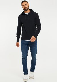 Felpa blu navy scura in maglia texture, con tasca anteriore e cordini regolabili. Abbinata a jeans blu e scarpe da tennis bianche.