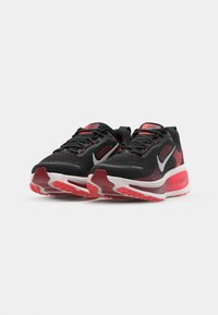 Chaussures de sport noires avec accents rouges, tige en mesh respirant, semelle rembourrée et unité d'air visible, avec un logo sur le côté et la languette.