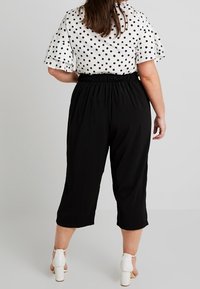 Czarne krótkie spodnie z elastycznym pasem, w połączeniu z białą bluzką w kropki, z krótkimi, falbanowymi rękawami.