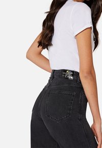 Džínové kalhoty s vysokým pasem v černé barvě s vybledlým vzhledem, dvě zadní kapsy a kožená nášivka se značkou na pásku. Měkká textura.