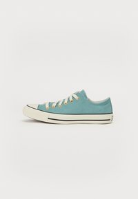 Light blue canvas sneaker with white rubber sole, tan laces, and black accent stripes along the sole. Rounded toe and metal eyelets.