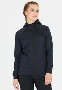 Svart zip-up huvtröja med en figurnära design, som har en huva, två sidofickor och flata sömmar för komfort. Tillverkad av ett mjukt, elastiskt tyg.