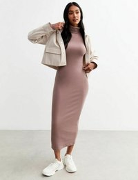 Robe longue mauve ajustée avec un col montant et une fente sur le côté, superposée avec une veste courte beige clair. Des baskets de sport blanches complètent le look.