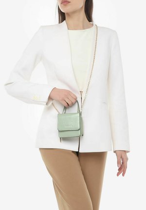 Mintgrønne croc-prægede crossbody taske med klaplukning, kort top-håndtag og kædestrop, båret sammen med en hvid blazer og beige bukser.