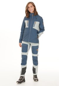 Buitenjas en broek in donkerblauw en lichtgrijs. Kenmerken zijn onder andere meerdere zakken, ritsen en gestructureerde accenten voor duurzaamheid.
