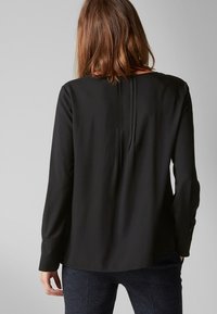 Blusa nera a maniche lunghe con scollatura rotonda, caratterizzata da una leggera piega sul retro e da una texture del tessuto liscia, progettata per una vestibilità morbida.