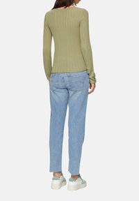 Hellgrünes, ribbeltes Langarmoberteil, kombiniert mit hellblauen Jeans und weißen Sneakers mit mintgrünen Akzenten.