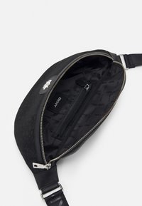 Černá taška přes rameno s texturovaným povrchem, stříbrným zipem a logem. Interiér obsahuje malou zipovou kapsu a podšívku s logem.