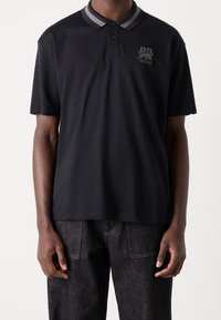 Zwarte polo met een bicolor grijze kraag, voorzien van een logo op de linkerborst. Gemaakt van een soepele stof met korte mouwen en een klassieke pasvorm.