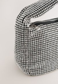 Rhinestone-embellished handbag featuring a structured shape, glossy black fabric base, and a zip closure with silver hardware.