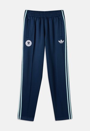 Αθλητικό παντελόνι σε ναυτικό μπλε με ανοιχτό μπλε ρίγες στο πλάι, ελαστική μέση, τσέπες με φερμουάρ και λευκό λογότυπο Adidas μαζί με το έμβλημα της Γερμανικής ποδοσφαιρικής ομάδας στο μπροστινό μέρος.