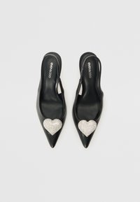 Musta nahkainen slingback-korkokengät, joissa on terävät varpaat ja suuret hopeiset kimallekivisydänkoristeet kummassakin kengässä.