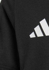 Czarny bawełniany t-shirt o gładkiej fakturze, z wyraźnym białym logo adidas składającym się z trzech ukośnych pasków na ramieniu.