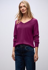 Pull en maille violette ajusté avec un col en V et des manches longues. Associé à un jean bleu foncé, doté de poches standard et d'un bouton en métal.