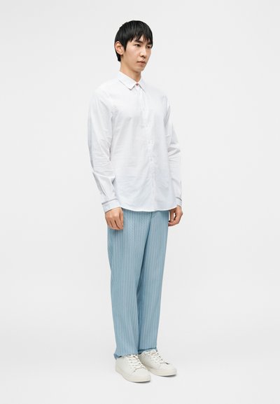 Άσπρο πουκάμισο με μακριά μανίκια και κουμπιά, ανοιχτό μπλε ριγέ παντελόνια και άσπρα αθλητικά παπούτσια. Λείο ύφασμα, εφαρμοστή γραμμή, casual σχεδίαση.