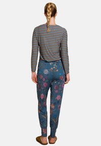 Gestreepte longsleeve top in meerdere kleuren; blauwe broek met bloemenprint en elastische taille; zachte stof; casual pasvorm; gecombineerd met beige slippers.