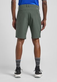 Shorts verts en matériau léger, dotés d'une taille plate, d'une coupe droite et de coutures contrastées, associés à des chaussettes grises.