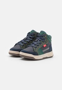 Zapatillas altas con tela azul marino y verde, paneles texturizados, costuras en contraste y una etiqueta de logo blanca en el lateral.