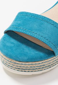 Tyrkysové semišové platformové sandály se širokým páskem a texturovanou jutovou mezipodešví, s bílým prošíváním a hladkým vnitřním podšíváním.