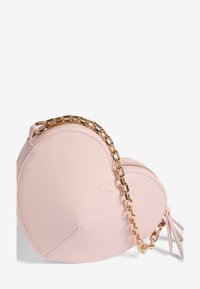 Ružová taška v tvare srdca vyrobená z hladkého materiálu, s zlatým reťazovým popruhom a zipsovým uzatvorením, s jemným logom na prednej strane.