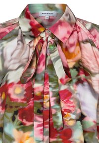 Floral patterned blouse with a ruffled collar, featuring shades of pink, red, green, and yellow. Textured fabric with a tie detail at the neck.