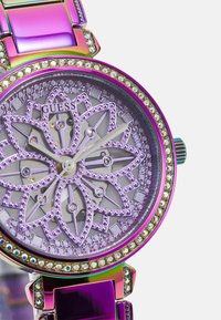 Guess-Uhr mit lila und metallischem Armband, blumenmuster Zifferblatt mit silberfarbenen Zeigern, verziert mit Kristallen um das Gehäuse.