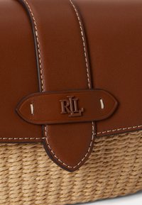 Rabatté en cuir marron avec couture blanche et fermoir embossé du logo "RL" sur une base de sac en osier tressé beige.