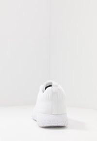 Valkoinen urheilukengä, jossa on neulottu päällinen, vetotankoa kantapäässä ja teksturoitu kumipohja. Minimalistinen muotoilu, sileä pinta, ei näkyviä logoja.