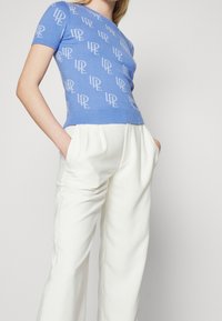 Maglione blu a maniche corte con ripetuto motivo logo "LR" grigio chiaro; colletto e orlo a coste. Abbinato a pantaloni bianchi a vita alta.