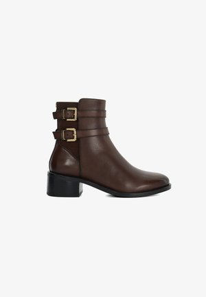 Botte chelsea en cuir marron avec deux sangles décoratives et boucles dorées, bout arrondi et un petit talon bloc pour plus de stabilité.