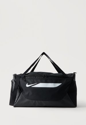Čierna športová taška Nike s bielym logom, hlavnou priehradkou na zips, predným vreckom a dvojitými nosnými pásmi na jednoliatom pozadí.