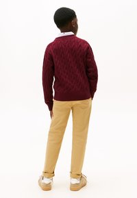 Maglione a trecce bordeaux con orlo a coste, abbinato a pantaloni khaki. Colletto bianco in vista, con sneakers casual alla base.