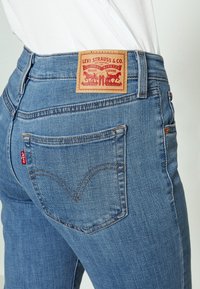 Jeans de mezclilla azul con cintura alta, con una etiqueta de cuero que dice "Levi Strauss & Co." y una pestaña roja característica en el bolsillo trasero.