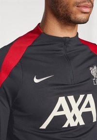 Schwarzes Sporttrikot mit roten Akzenten, weißem Nike-Swoosh und großem weißen "AXA"-Logo. Verfügt über einen hohen Kragen und ein leichtes Material.