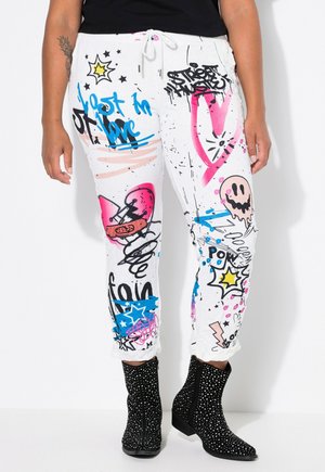 Bílé tepláky s vzory, pokryté barevnými graffiti designy v růžové, modré a černé, s páskem na stažení a elastickými manžetami.